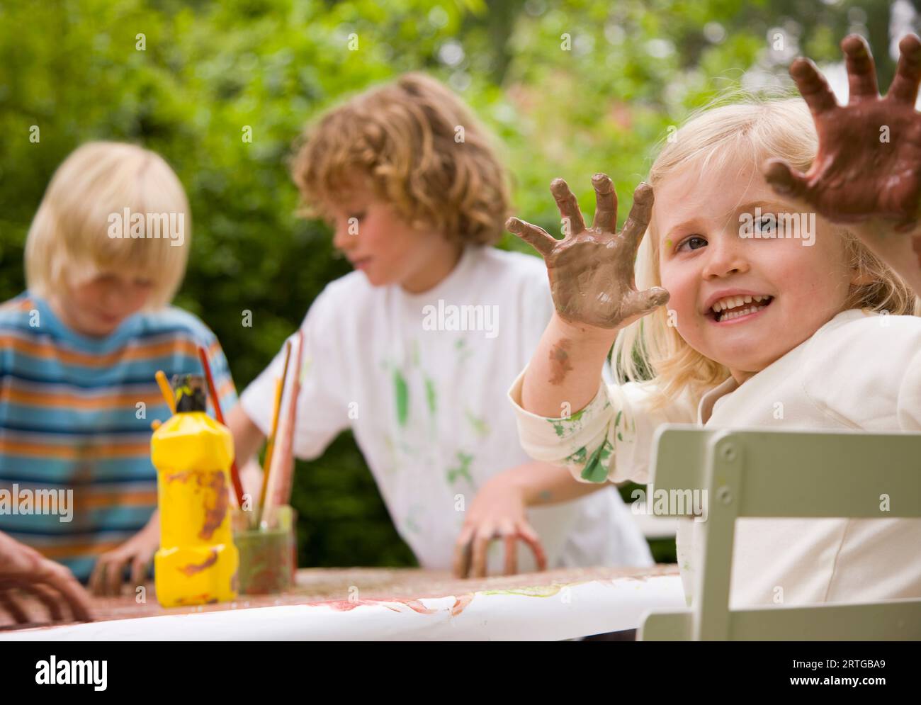 Junges Mädchen am Tisch hält Arme mit Händen bedeckt in Farbe Stockfoto