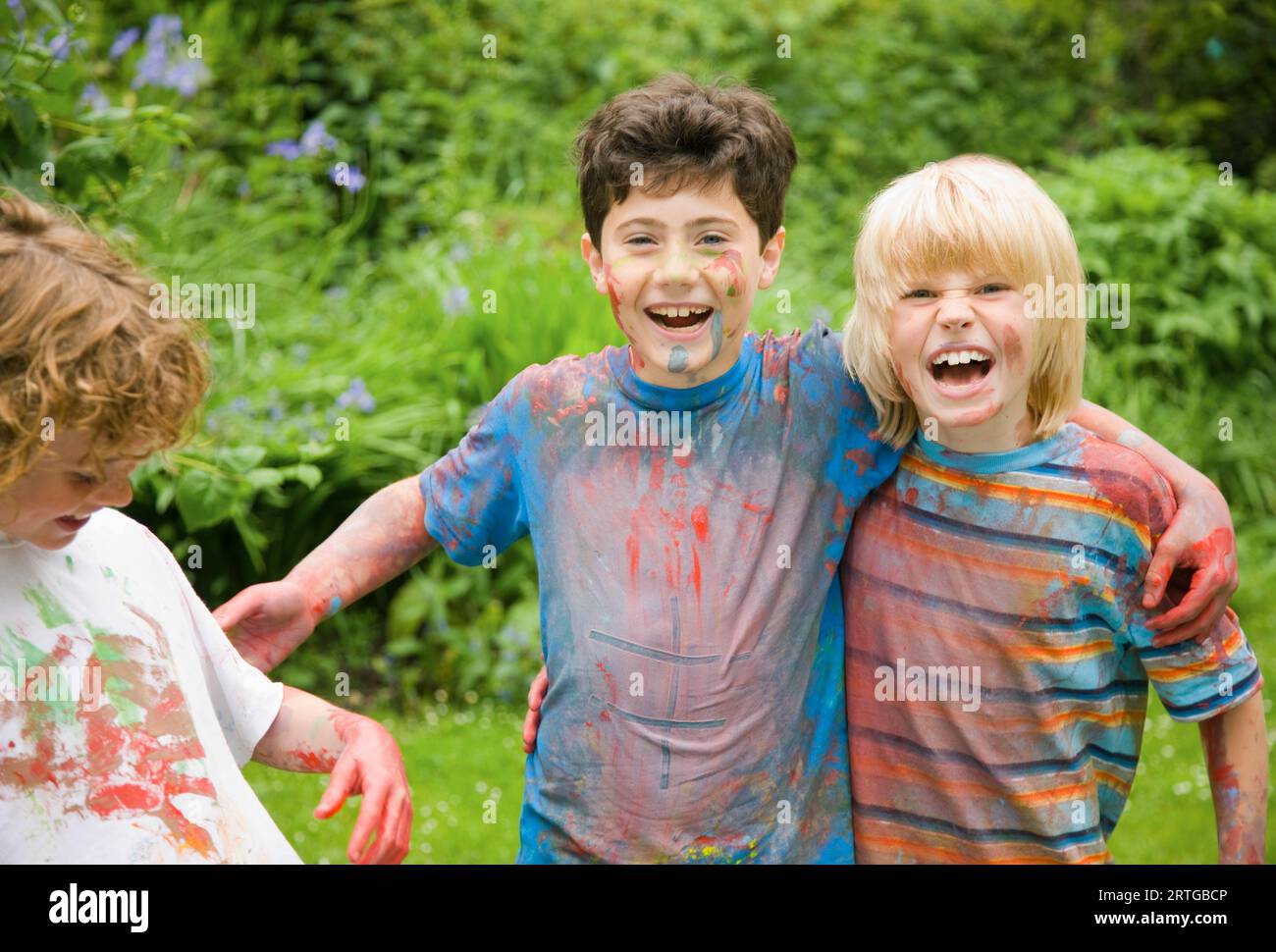 Junge, die mit Aquarellfarbe bedeckt sind, lachen im Garten Stockfoto