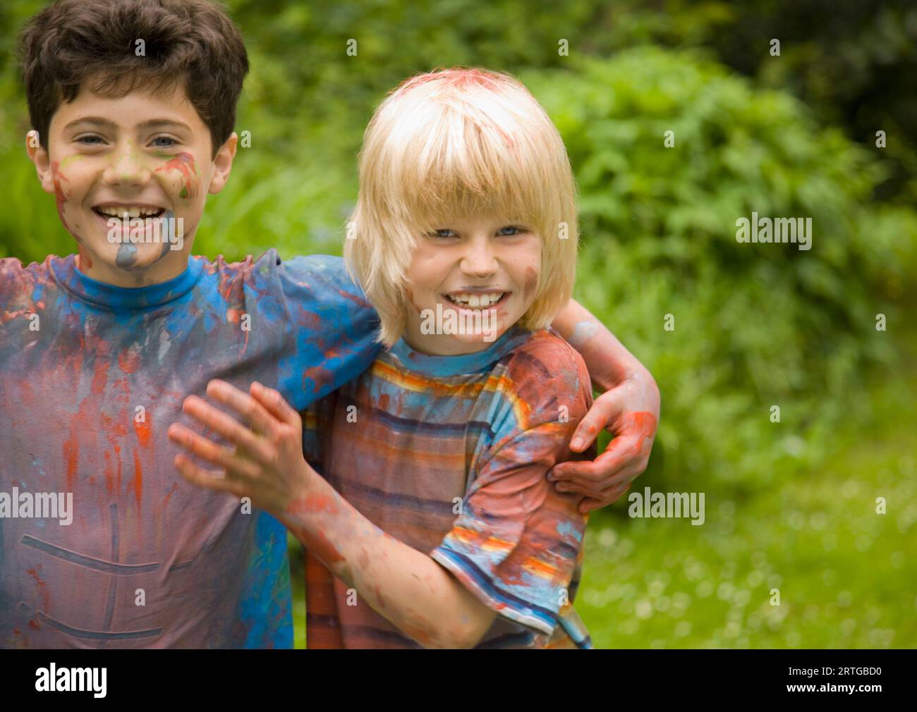 Zwei junge Jungs, die mit Aquarellfarbe bedeckt sind, lachen im Garten Stockfoto