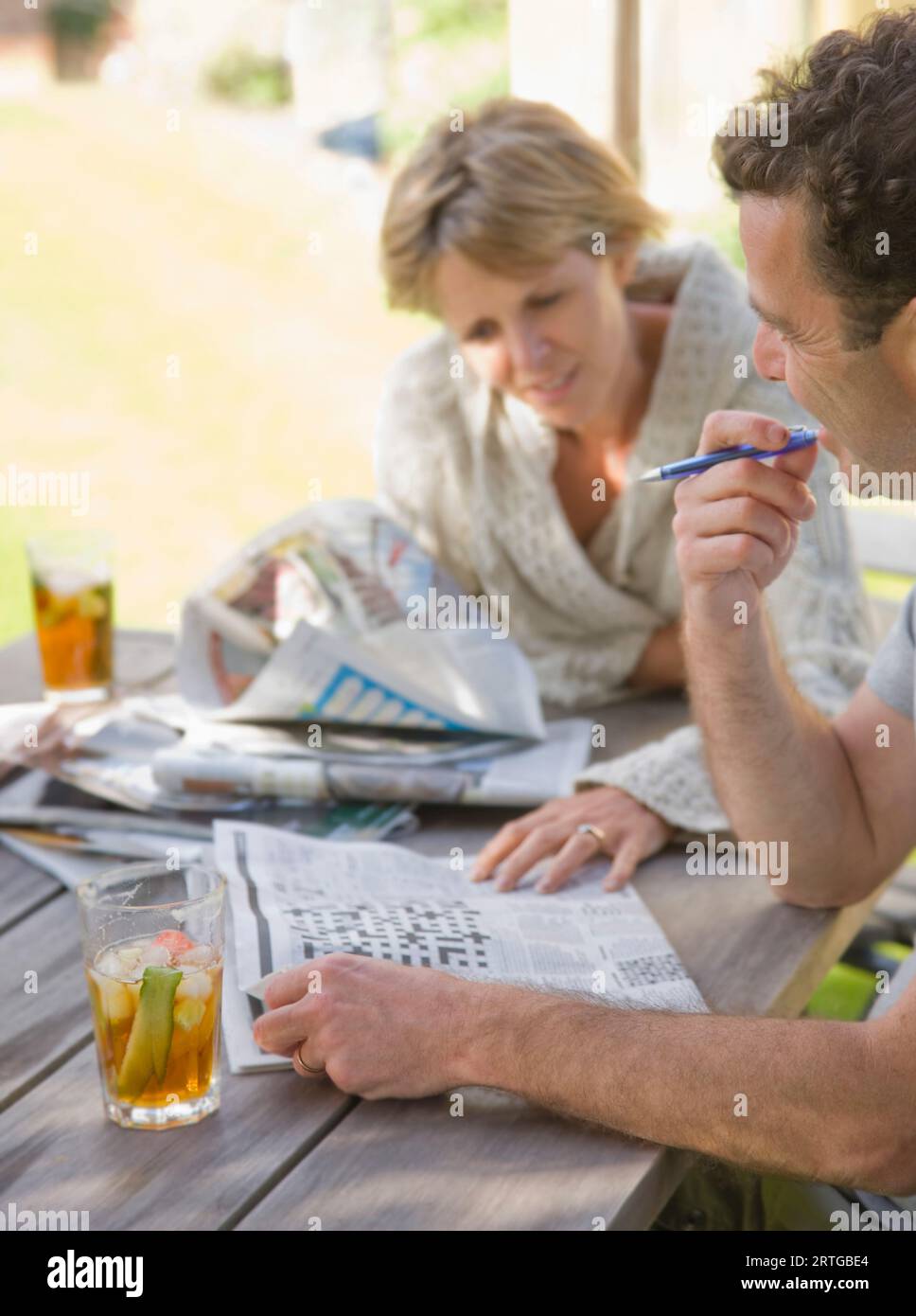 Ein Paar sitzt draußen und trinkt Cocktails und macht Kreuzworträtsel Stockfoto