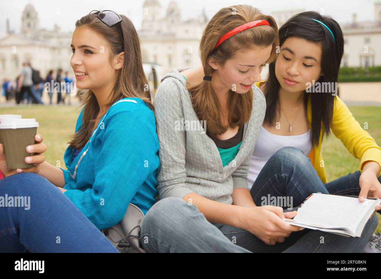 Mädchen im Teenageralter sitzen vor der London Horse Guards Parade, trinken Kaffee und lesen ein Buch Stockfoto