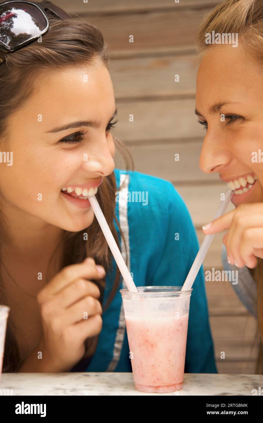 Zwei lächelnde Teenager Mädchen trinken Milch-Shake mit einem Strohhalm aus demselben Glas Stockfoto
