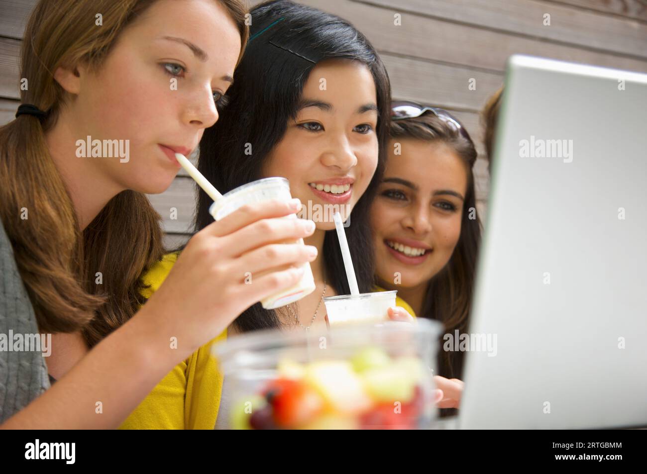 Mädchen im Teenageralter, die ihren Laptop benutzen, trinken Milchshake Stockfoto