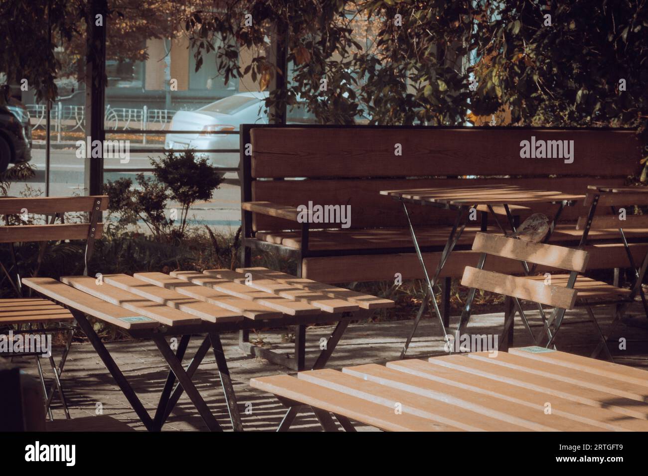Straßencafe. Moderner öffentlicher Ort in der Stadt. Holzstühle und -Tisch auf der Terrasse unter den Bäumen. Gartenmöbel. Moderne Lebensstile. Terrassendekoration. Stockfoto