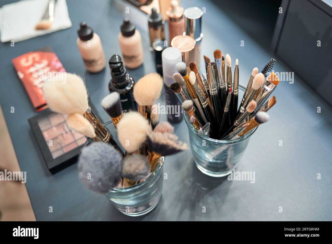 Von oben Sammlung von verschiedenen kosmetischen Bürsten in Gläsern auf dem Tisch mit verschiedenen Make-up-Produkten im modernen Schönheitssalon Stockfoto