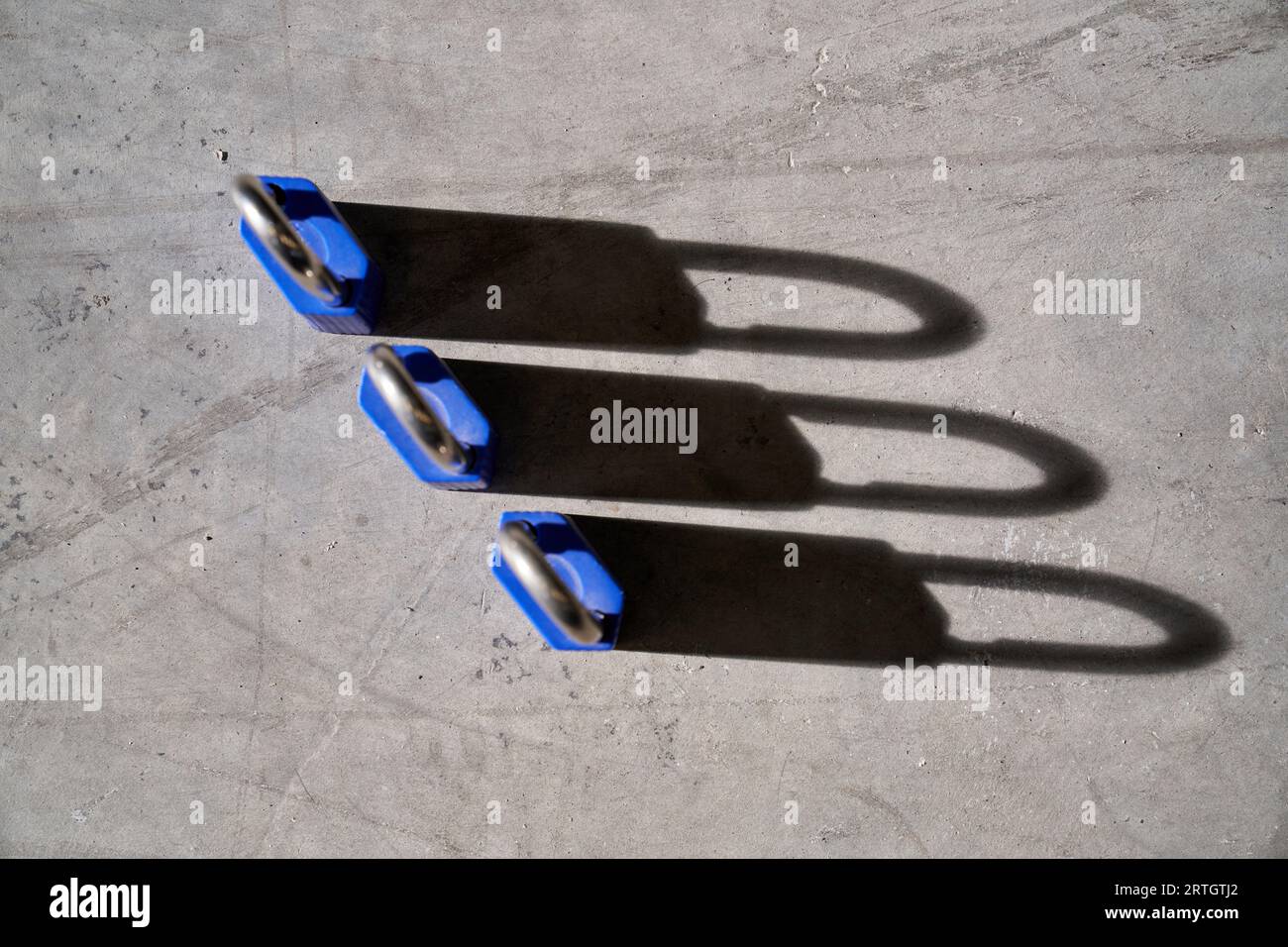 Draufsicht auf ähnliche blaue Vorhängeschlösser aus Eisen, die auf grauer, schäbiger Oberfläche mit Schatten im Sonnenlicht platziert sind Stockfoto