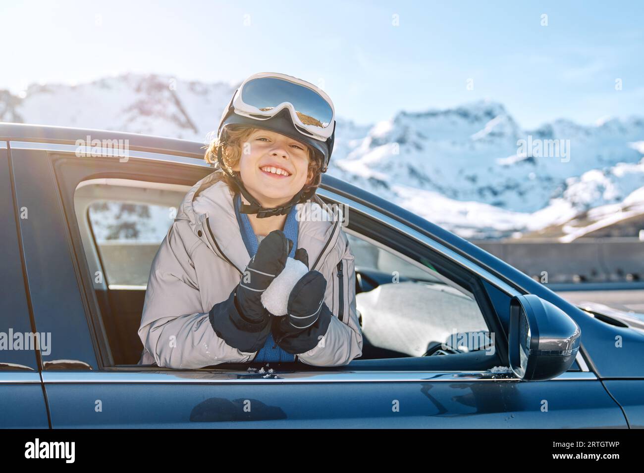 Begeistert war der Junge in der Skibrille, der die Kamera betrachtete, während er sich während des Roadtrips am Wintertag aus dem Autofenster mit Schneeball lehnte Stockfoto