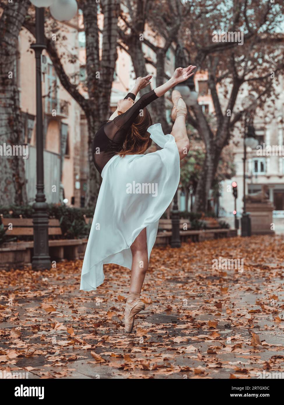 Seitenansicht der bezaubernden, nicht erkennbaren Ballerina in elegantem weißen Rock, der im Herbst auf der Straße geteilt auf verschwommenem Hintergrund steht Stockfoto