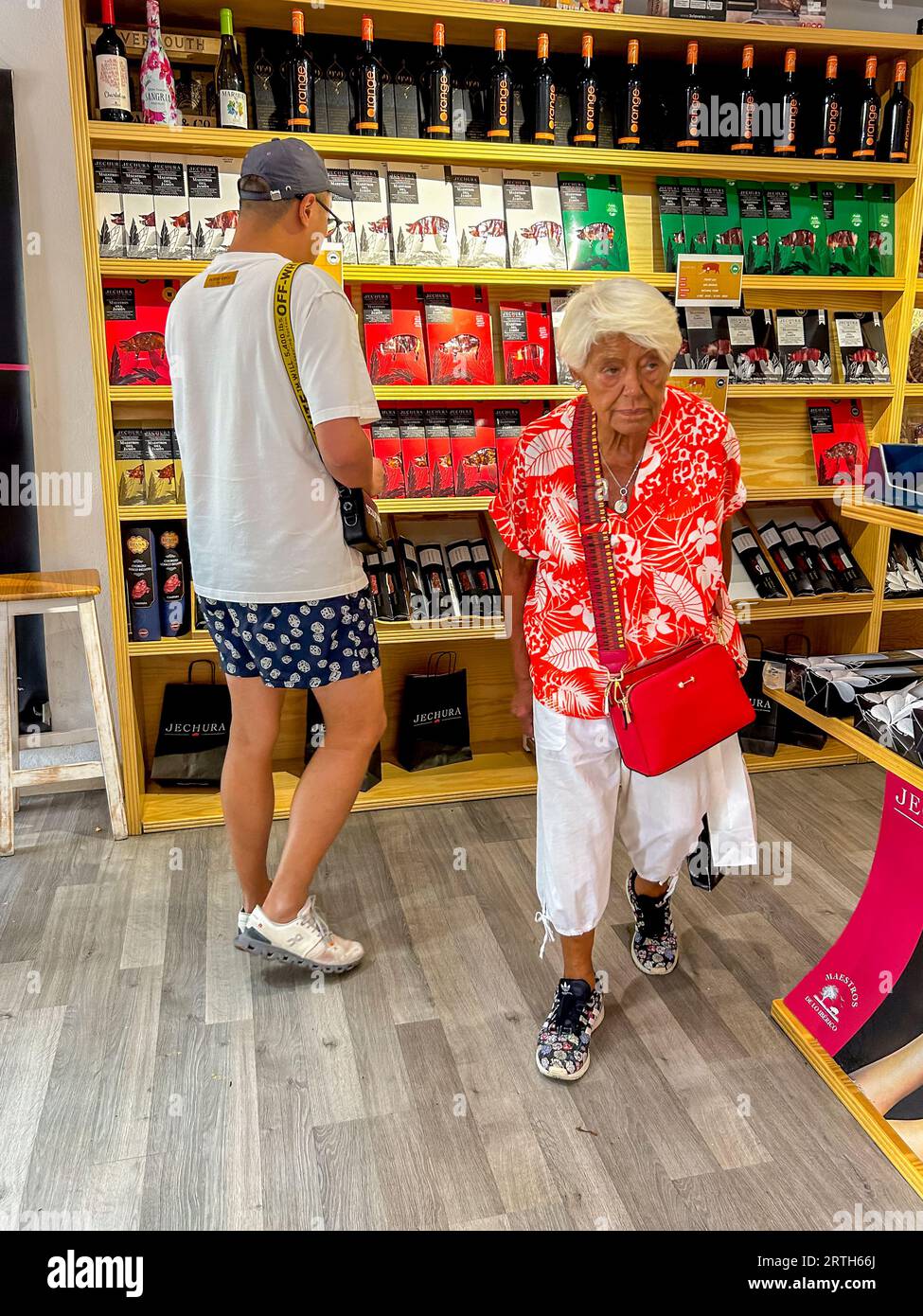 Sevilla, Spanien, Chinesischer Touristeneinkauf im traditionellen Spanischen Ham Store, Auswahl von Lebensmittelprodukten im Display, Alte Frau zu Fuß Stockfoto