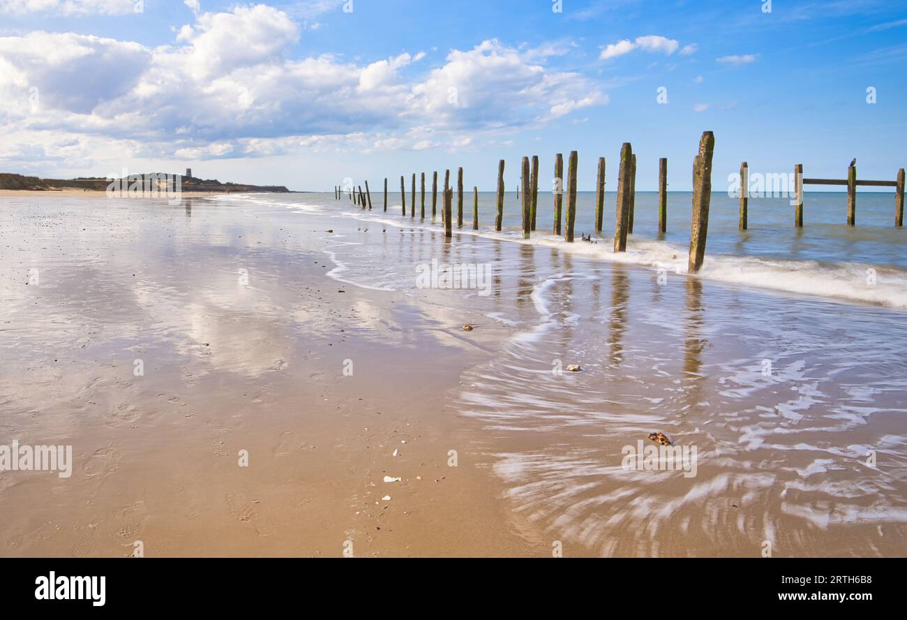 Die einfallenden Gezeiten durchziehen den wunderschönen goldenen Sand am Happisburgh Beach mit seinen markanten Holzpfählen, die den Meeresrand säumen. Stockfoto