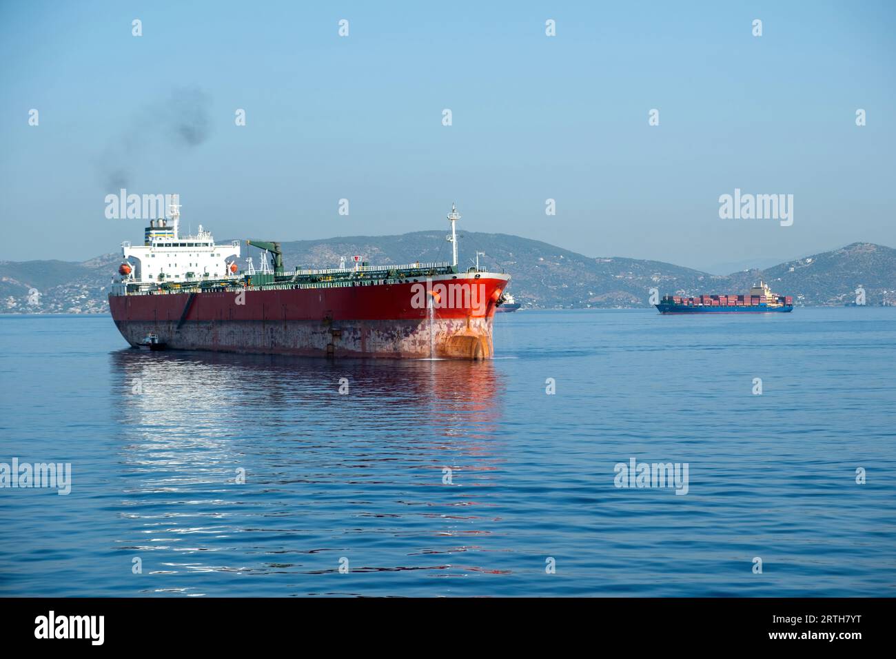 Das beladene Containerfrachtschiff verlässt den Hafen von Piräus, Griechenland. Import von Exportgeschäften und Logistik. Rauch vom Schiffschornstein, Meer, blauer Himmel Hintergrund. Stockfoto