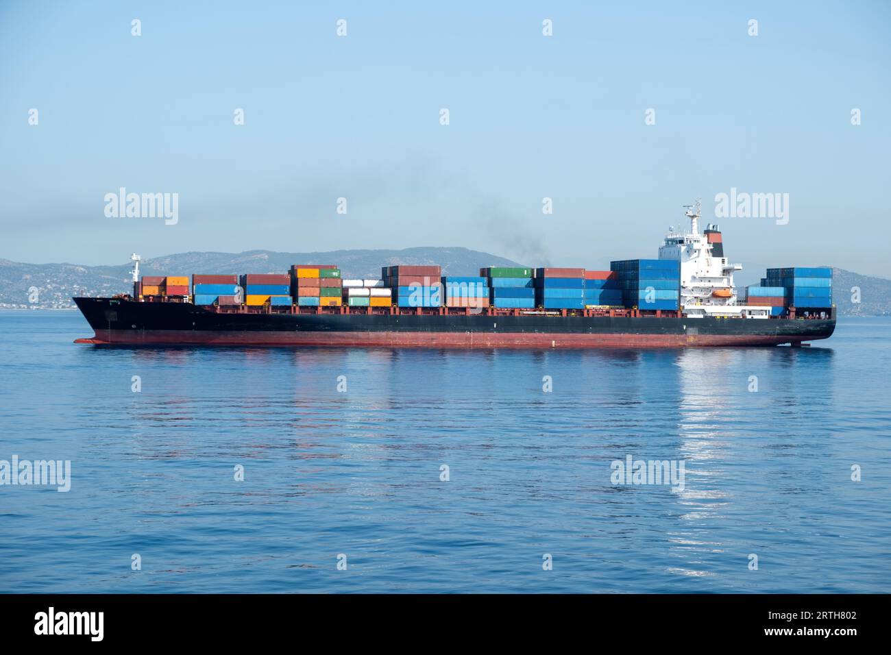 Das beladene Containerfrachtschiff verlässt den Hafen von Piräus in Griechenland. Lagerung und Transport von schweren Waren für Import und Export. Reflexion im Mittelmeer. Stockfoto