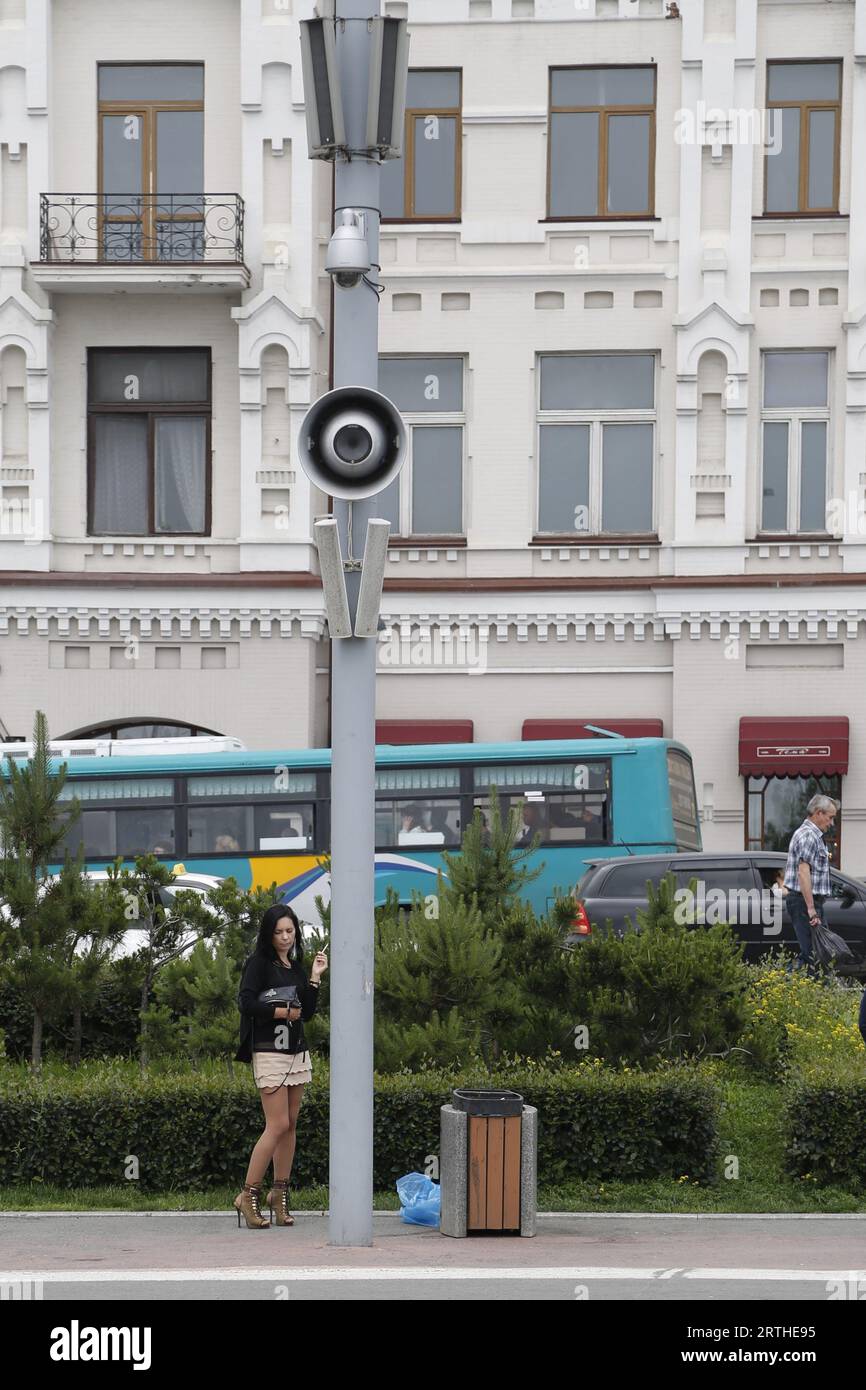 Straßenpfosten mit Lautsprechern und Kamera; Konzept zur Überwachung, Massenüberwachung, Kontrolle im öffentlichen Bereich. Eine Frau steht daneben und raucht eine Zigarette Stockfoto