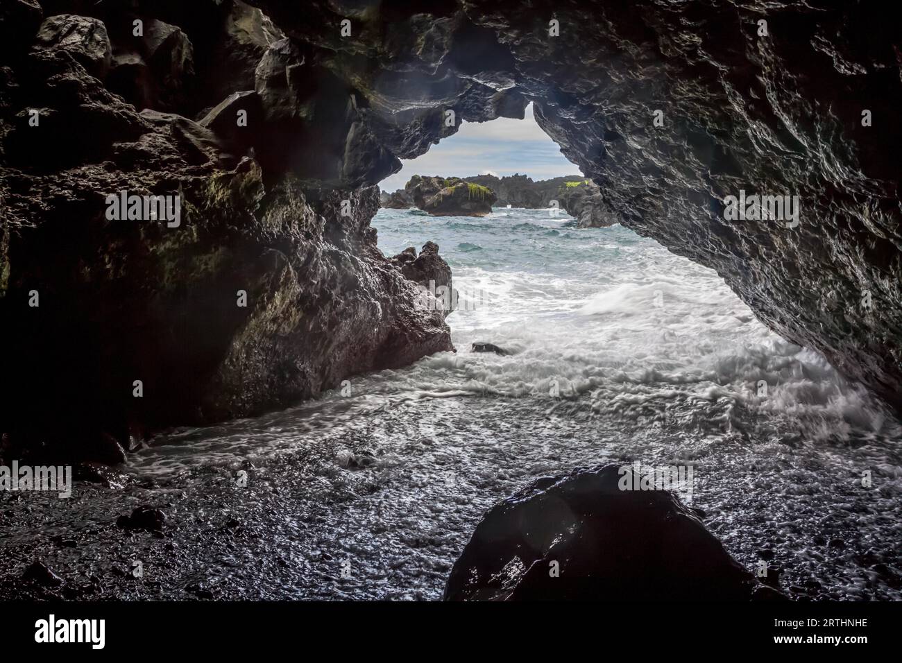 Der Surf läuft in eine Höhle am Waianapanapa Black Sand Beach in der Nähe von Hana auf Maui, Hawaii, USA Stockfoto