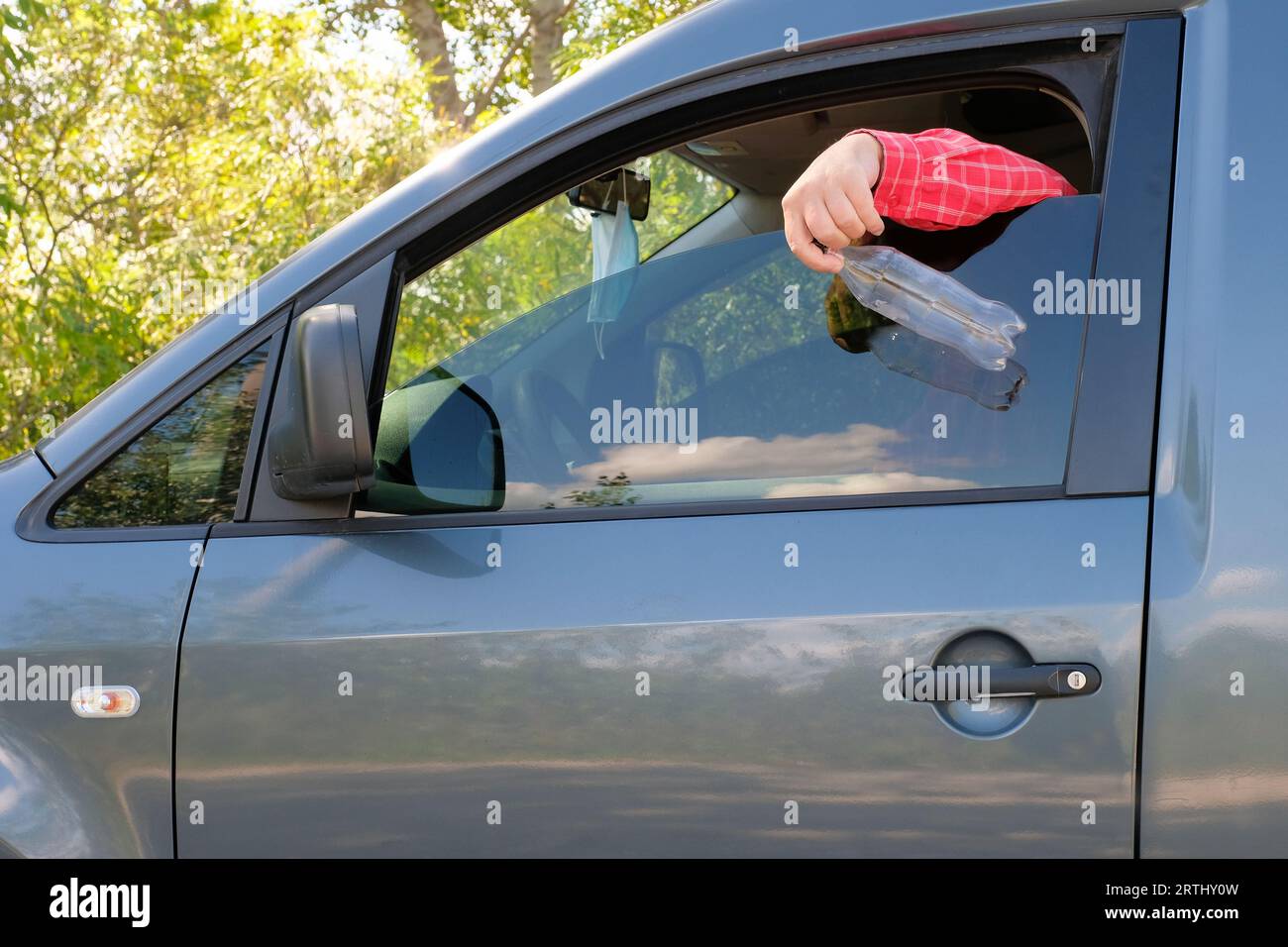 Der Fahrer wirft eine Plastikflasche aus dem Autofenster. Müll auf der Straße. Stockfoto
