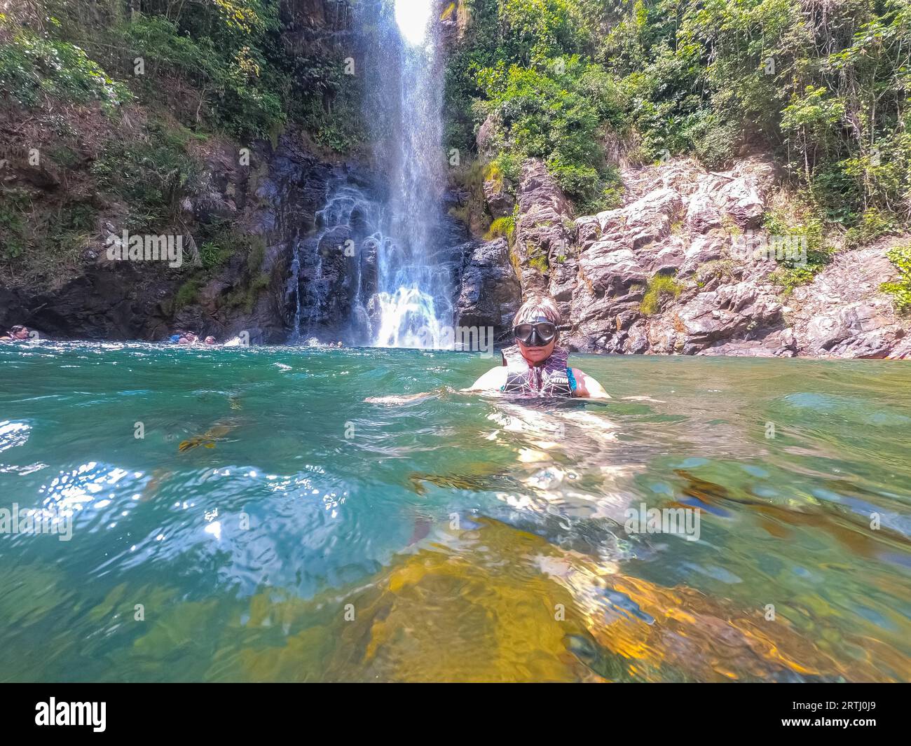 Vorderansicht des Schnorchlers, Kopf aus dem Wasser, beobachten Fische um sie herum, tropischer Wasserfall im Hintergrund Stockfoto