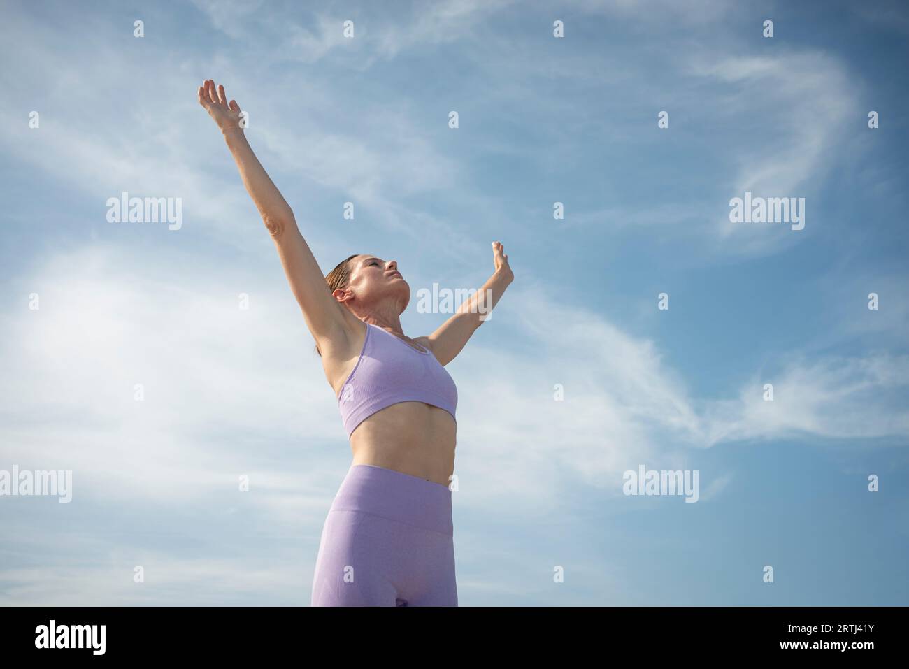 Sportliche Frau mit erhobenen Armen vor blauem Himmel. Stockfoto