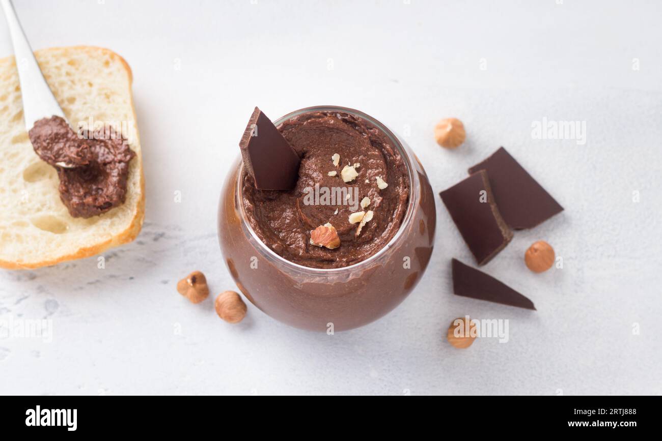 Vegane Schokoladenpaste mit Bananen und Nüssen, umgeben von Zutaten: Schokolade und Haselnüsse auf hellgrauem Hintergrund, Draufsicht Stockfoto