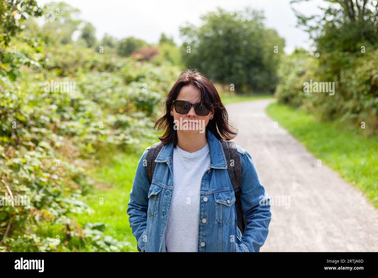 Porträt einer schönen Frau mittleren Alters in einer Jeansjacke und Sonnenbrille auf einer Landstraße Stockfoto