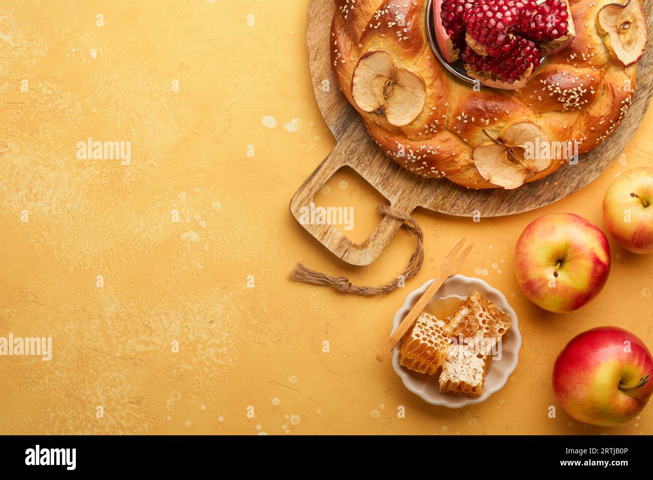 Jüdische Feiertage - Rosh Hashanah oder Rosh Hashana. Granatäpfel, Äpfel, Honig und runde Challah auf rustikalem gelbem Tischhintergrund. Jüdisches Herbstfest Stockfoto