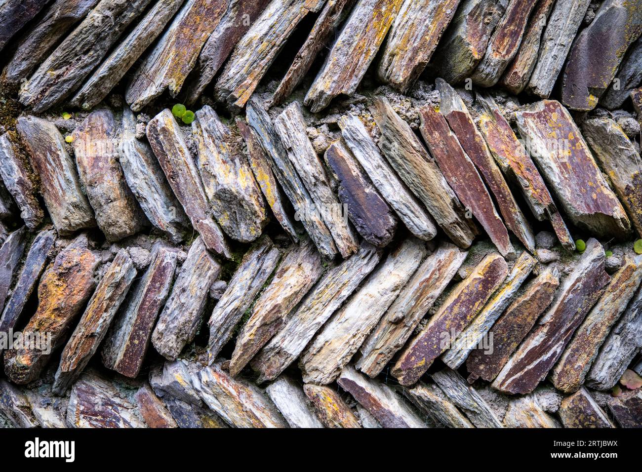 Abstrakte Steine, die in einem Fischgrätenmuster gelegt wurden, um eine Trockensteinmauer zu schaffen Stockfoto