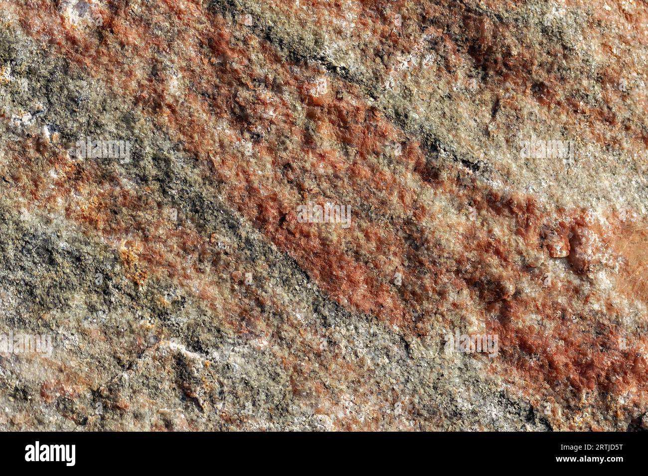 Granitsteinoberfläche mit Rauheit und Unebenheit mit roten und grauen Aderungen als abstrakter Hintergrund und Textur. Stockfoto