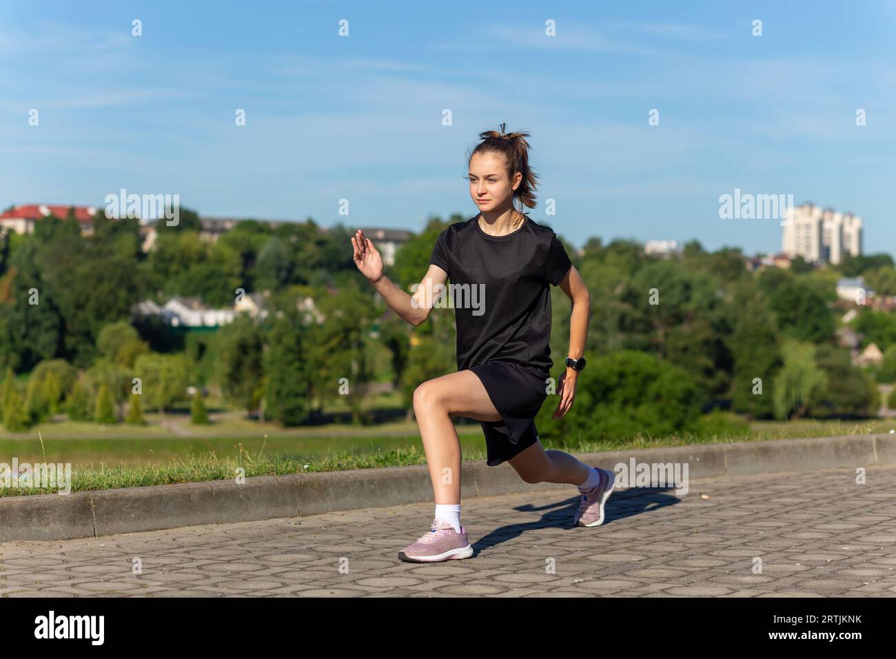 Junges, fittes und sportliches Mädchen in schwarzer Kleidung, das sich nach dem Workout im Stadtpark ausdehnt. Fitness, Sport, Urban Jogging und gesunder Lebensstil c Stockfoto