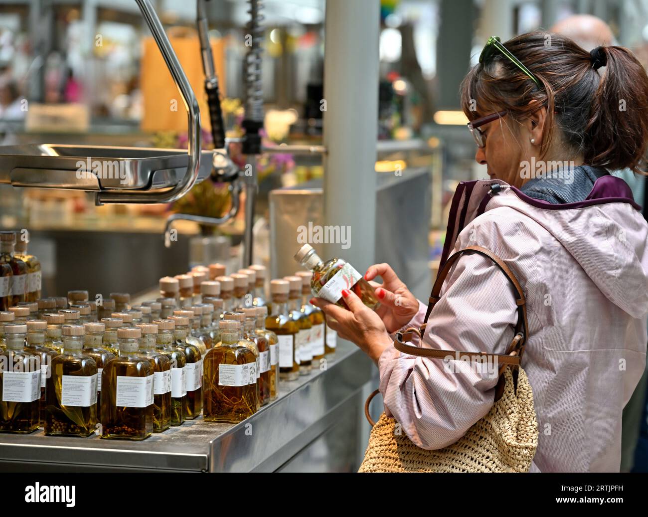 Frau, die ein Glas Olivenöl mit Kräutern und Gewürzen für das Segeln untersucht Stockfoto