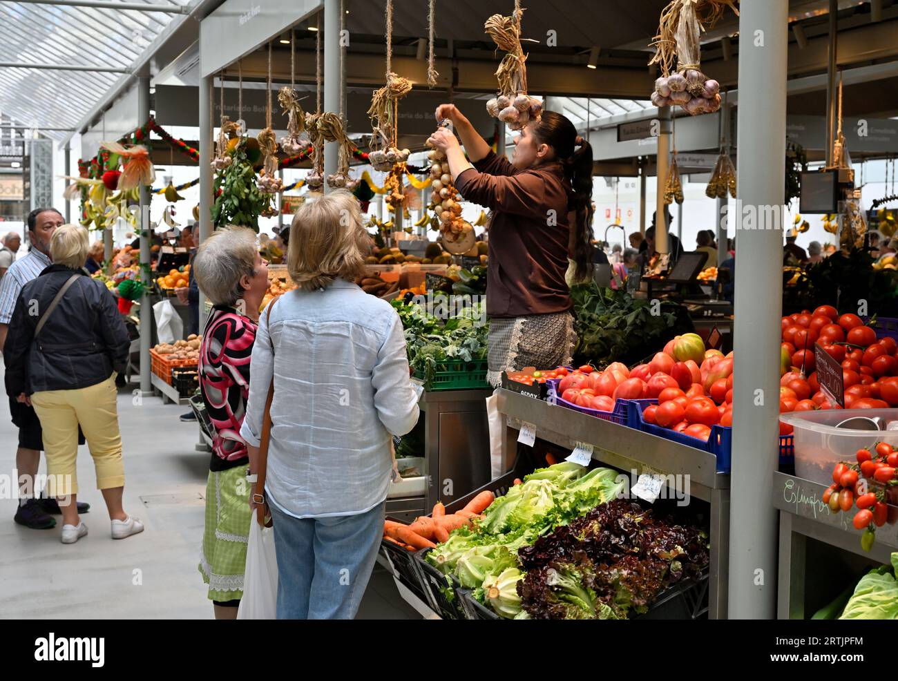 Marktstand, der eine Mischung aus frischem Gemüse verkauft, und Anbieter, der Knoblauchfäden abhakt, mit Kunden, die danach suchen Stockfoto