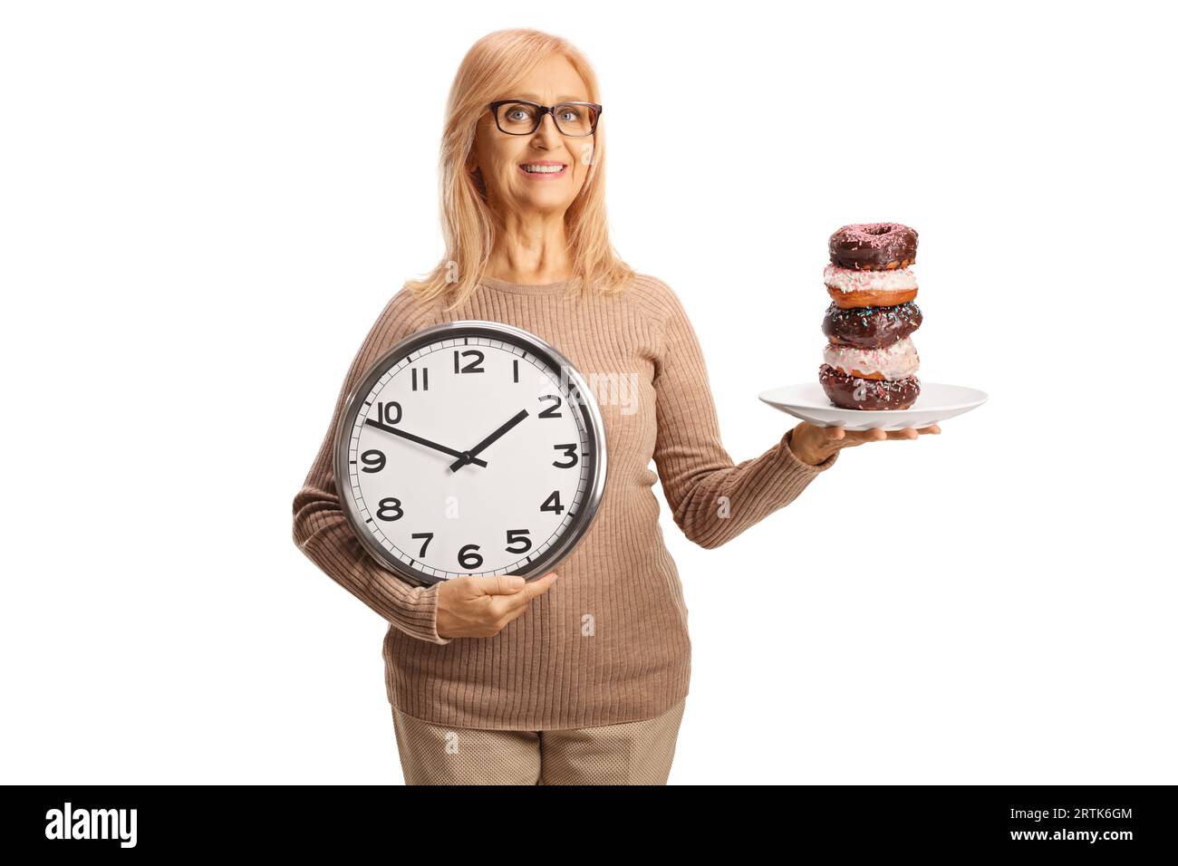 Reife Frau, die Donuts auf einem Teller und eine Uhr auf weißem Hintergrund hält Stockfoto