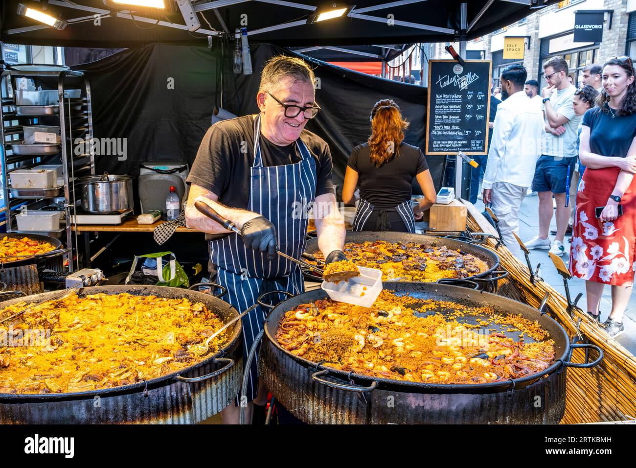 A man Serves Paella at A Street Food Stall, Berwick Street, London, UK. Stockfoto