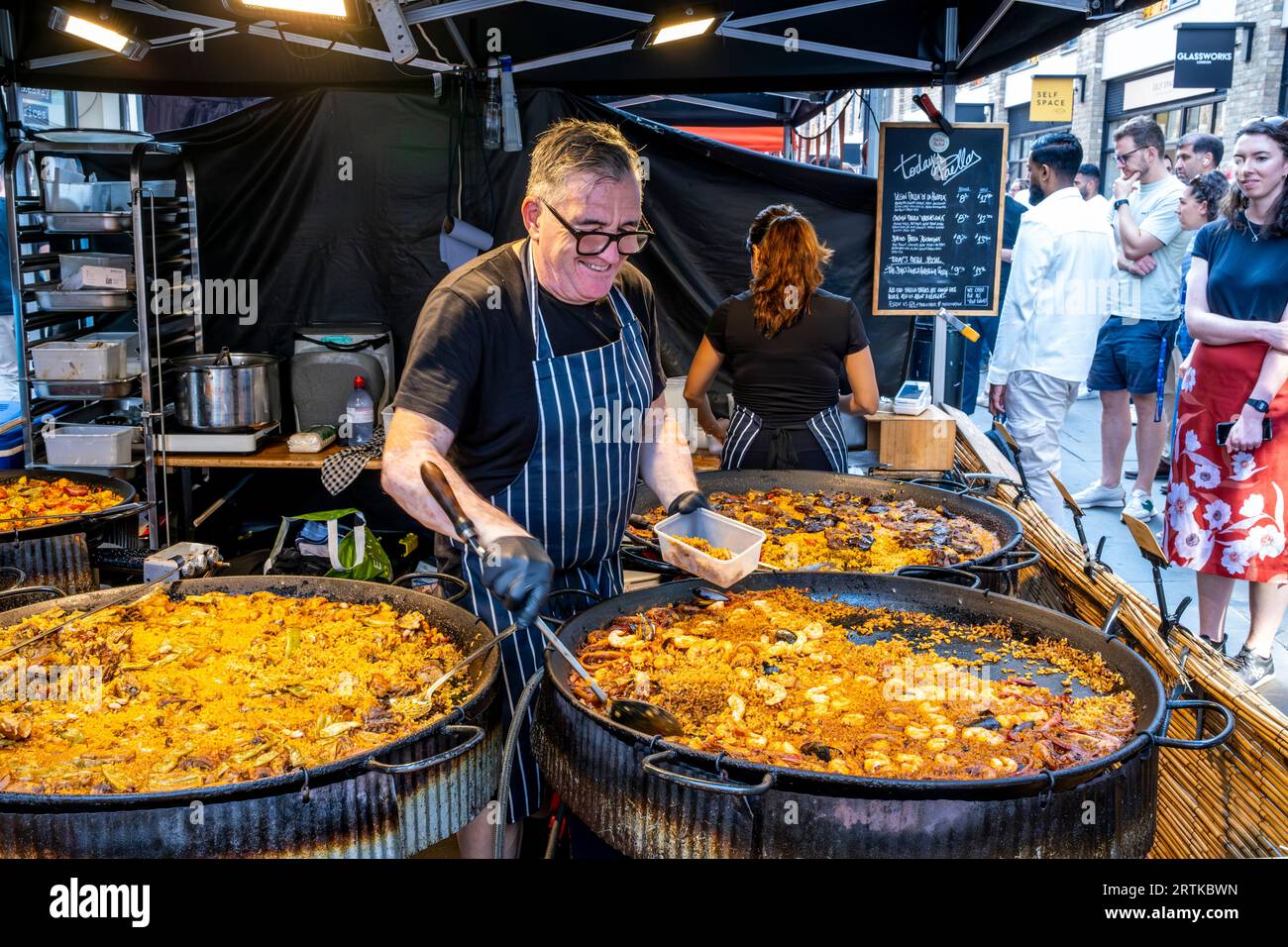 A man Serves Paella at A Street Food Stall, Berwick Street, London, UK. Stockfoto