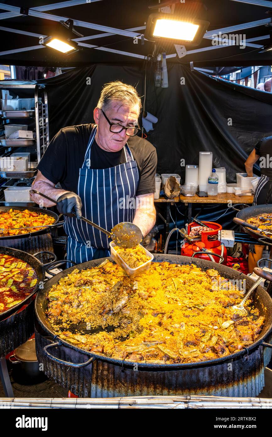 A man Serves Paella at A Street Food Stall, Berwick Street, London, UK. Stockfoto