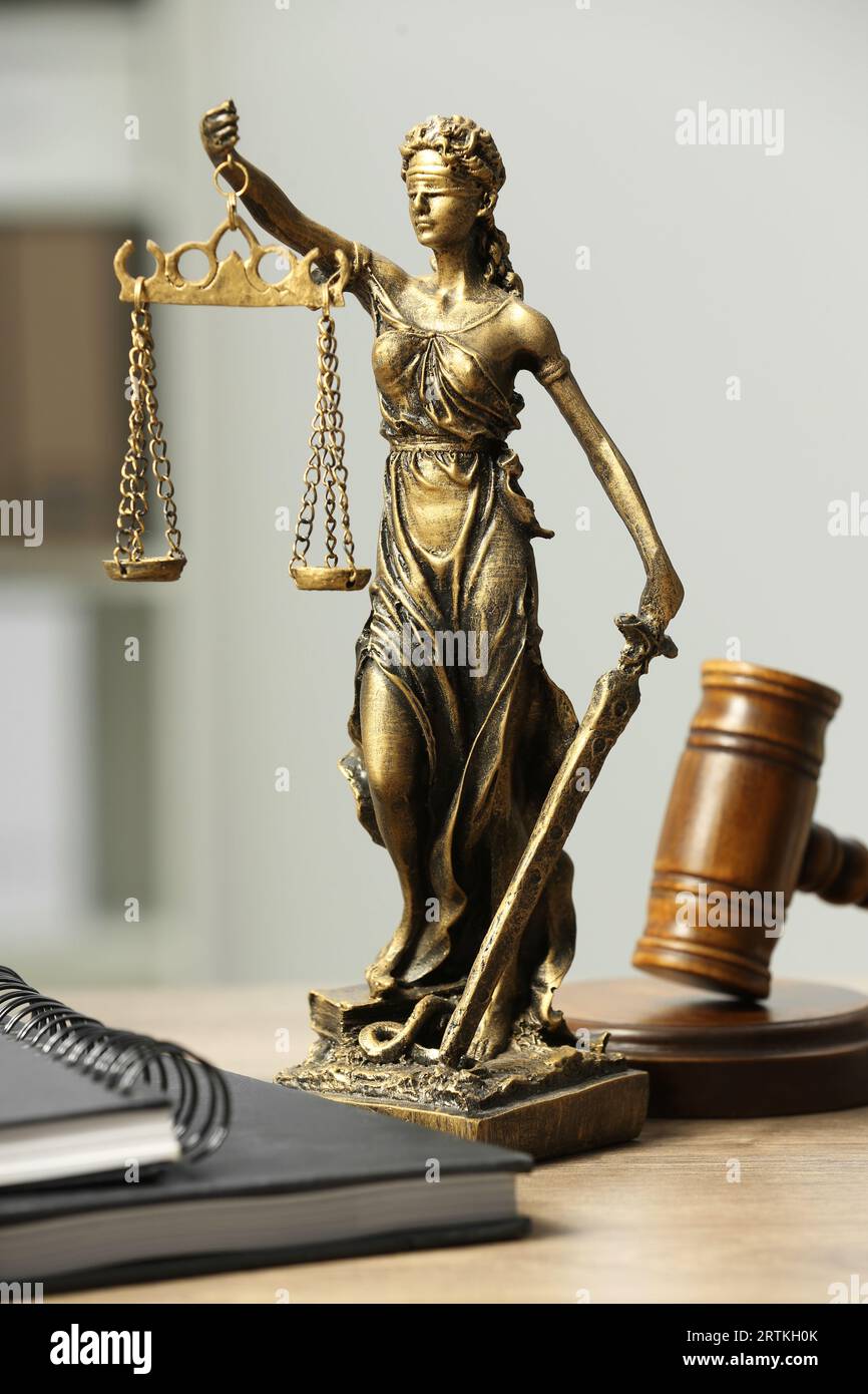 Figur der Lady Justice, Hammer und Notizbücher auf Holztisch im Innenbereich. Symbol der gerechten Behandlung nach dem Gesetz Stockfoto