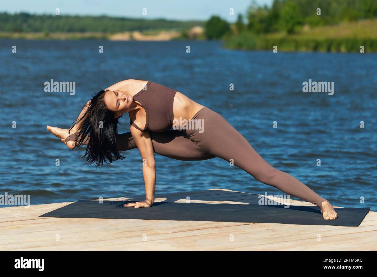 Frau, die Yoga praktiziert, Ardha Visvamitrasana-Übung durchführt, Salbei-Pose, allein in Sportbekleidung am Ufer eines Sees an einem sonnigen Tag trainiert Stockfoto