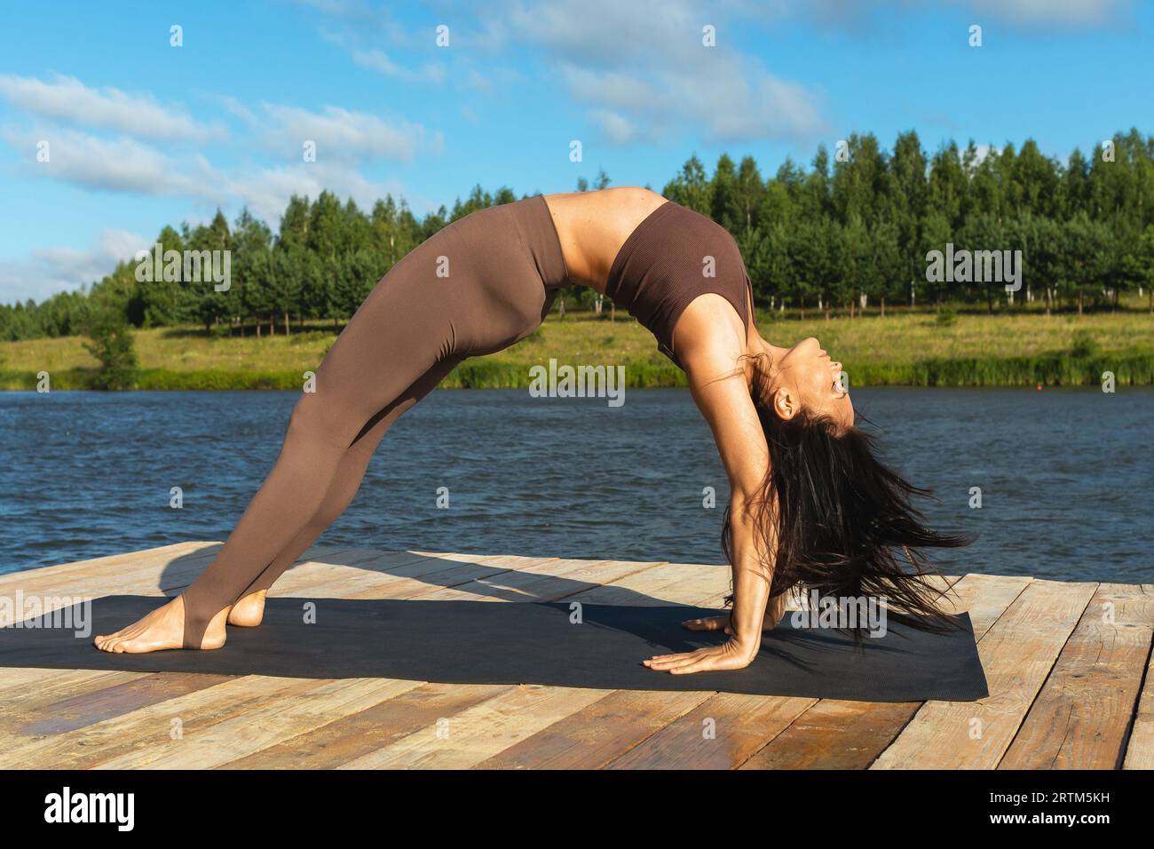 Frau, die Yoga macht, Setu Bandhasana-Übungen durchführt, Brückenstellung, alleine in Sportkleidung am Ufer eines Sees an einem sonnigen Morgen trainiert Stockfoto