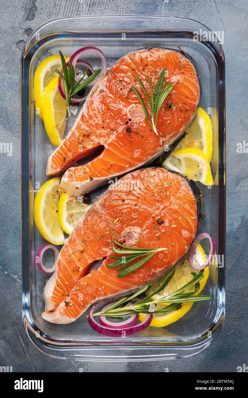 Zwei Steaks mit frischem rohem Rotfisch aus der Lachsfamilie, Forellenstücke mit verschiedenen Zutaten in einer durchsichtigen Glasform auf dem Tisch, Draufsicht Stockfoto