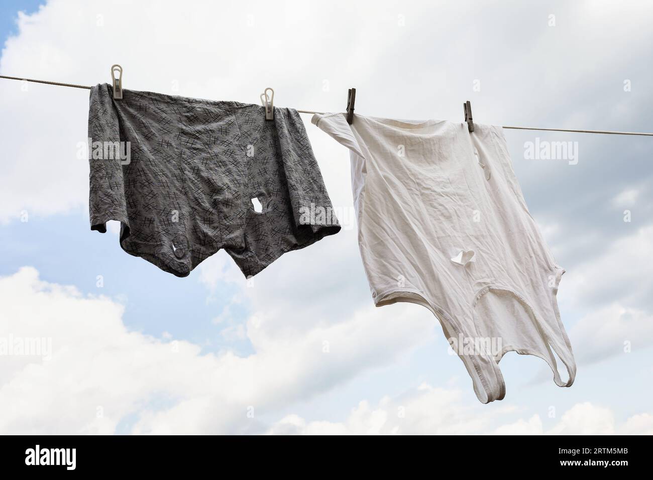 Ein undichtes Tanktop und Unterhosen hängen an einer Wäscheleine vor einem Wolkenhimmel, ein Konzept zum Thema Armut Stockfoto