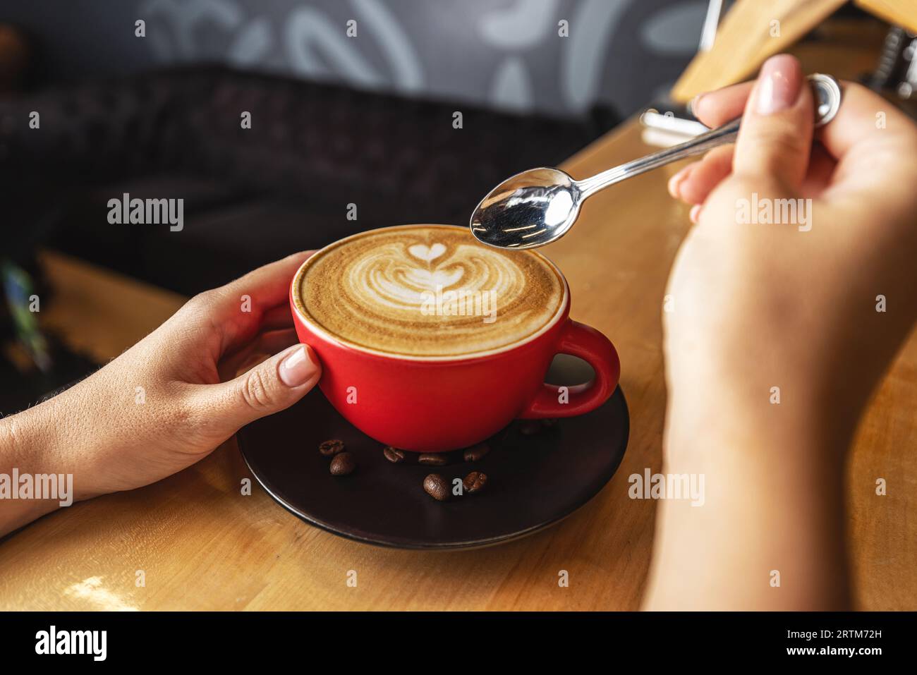 Hände einer Frau, die eine Tasse Cappuccino mit Kaffeekunst hält Stockfoto