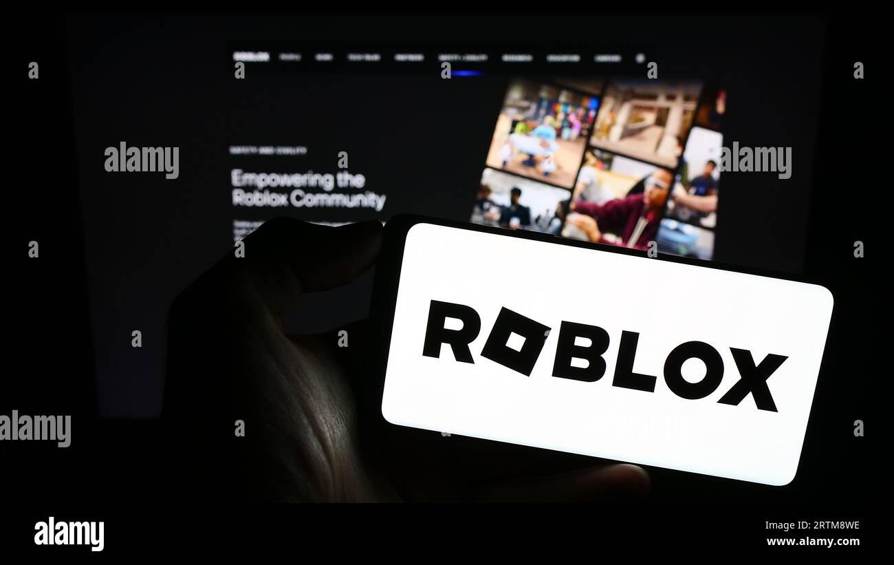 Person, die ein Mobiltelefon mit dem Logo der amerikanischen Videospielfirma Roblox Corporation auf dem Bildschirm vor der Webseite hält. Konzentrieren Sie sich auf das Display des Telefons. Stockfoto