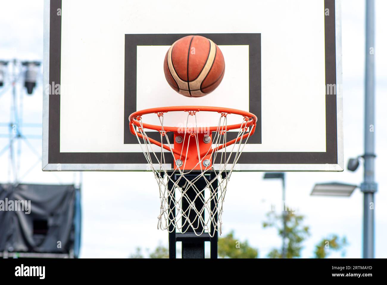 Basketballball tritt in den Korb ein. Vorderansicht von der Spielerposition, die auf der Straße auf dem Platz im Freien spielt Stockfoto