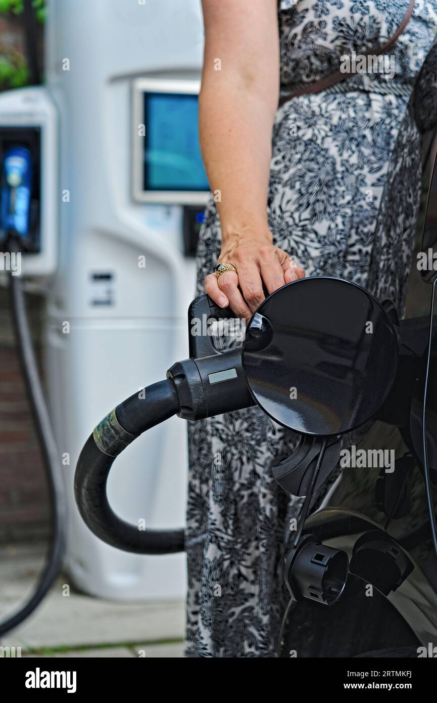 Die Buchse hält den Ladestecker und lädt das Elektroauto an einer EV-Ladestation an der Tankstelle auf. Ladebildschirm im Hintergrund. Umweltfreundlich Stockfoto