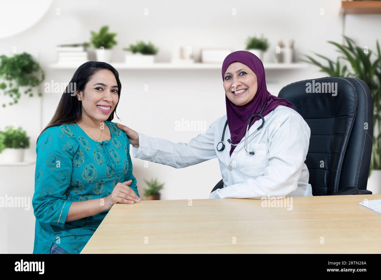 Junge indianerin berät über ihr Problem mit muslimischer Frauenärztin, die Hijab in einer modernen Klinik trägt. Blick auf die Kamera. Stockfoto