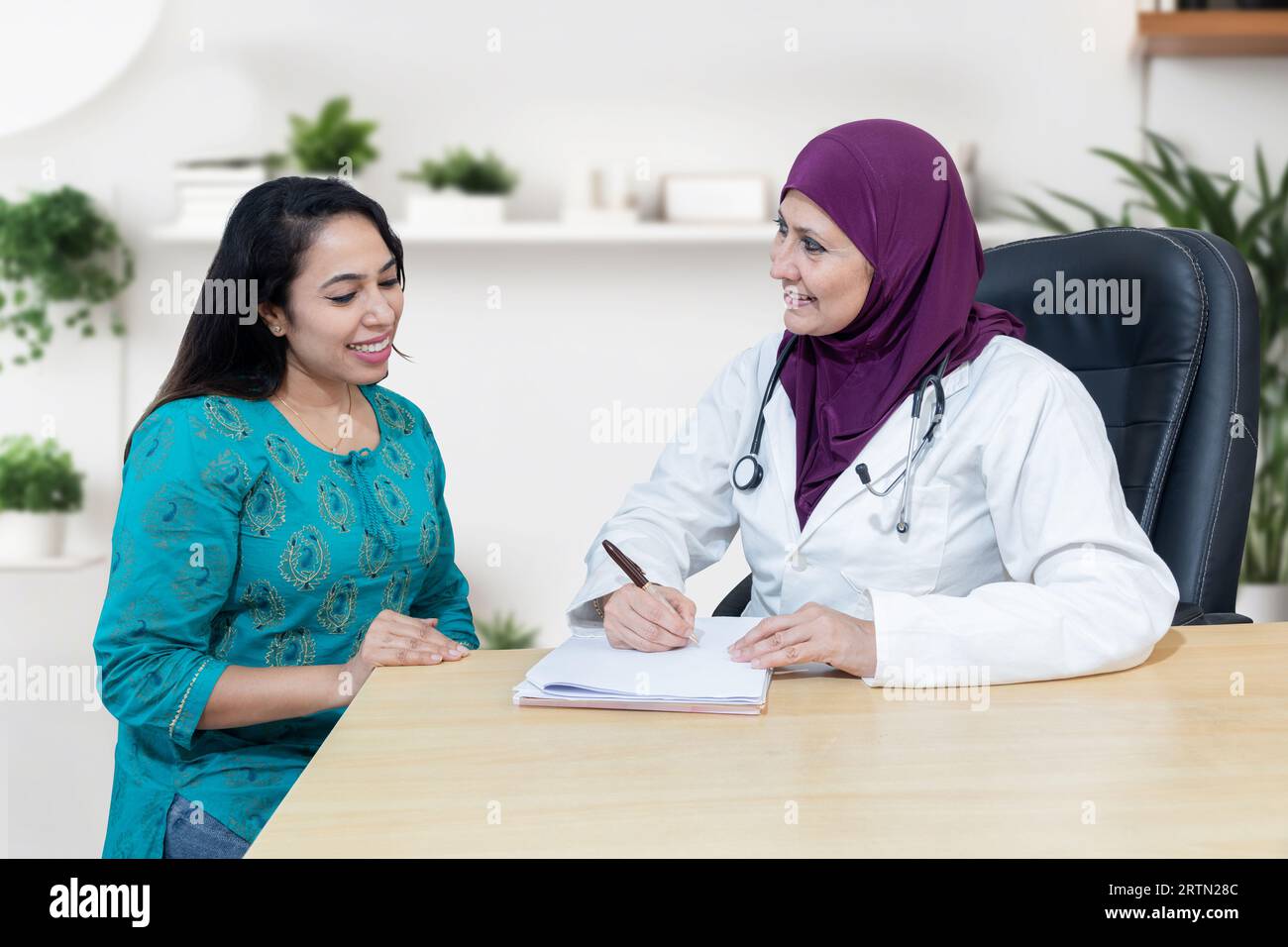 Junge indianerin berät über ihr Problem mit muslimischer Ärztin, die Hijab in einer modernen Klinik trägt. Stockfoto