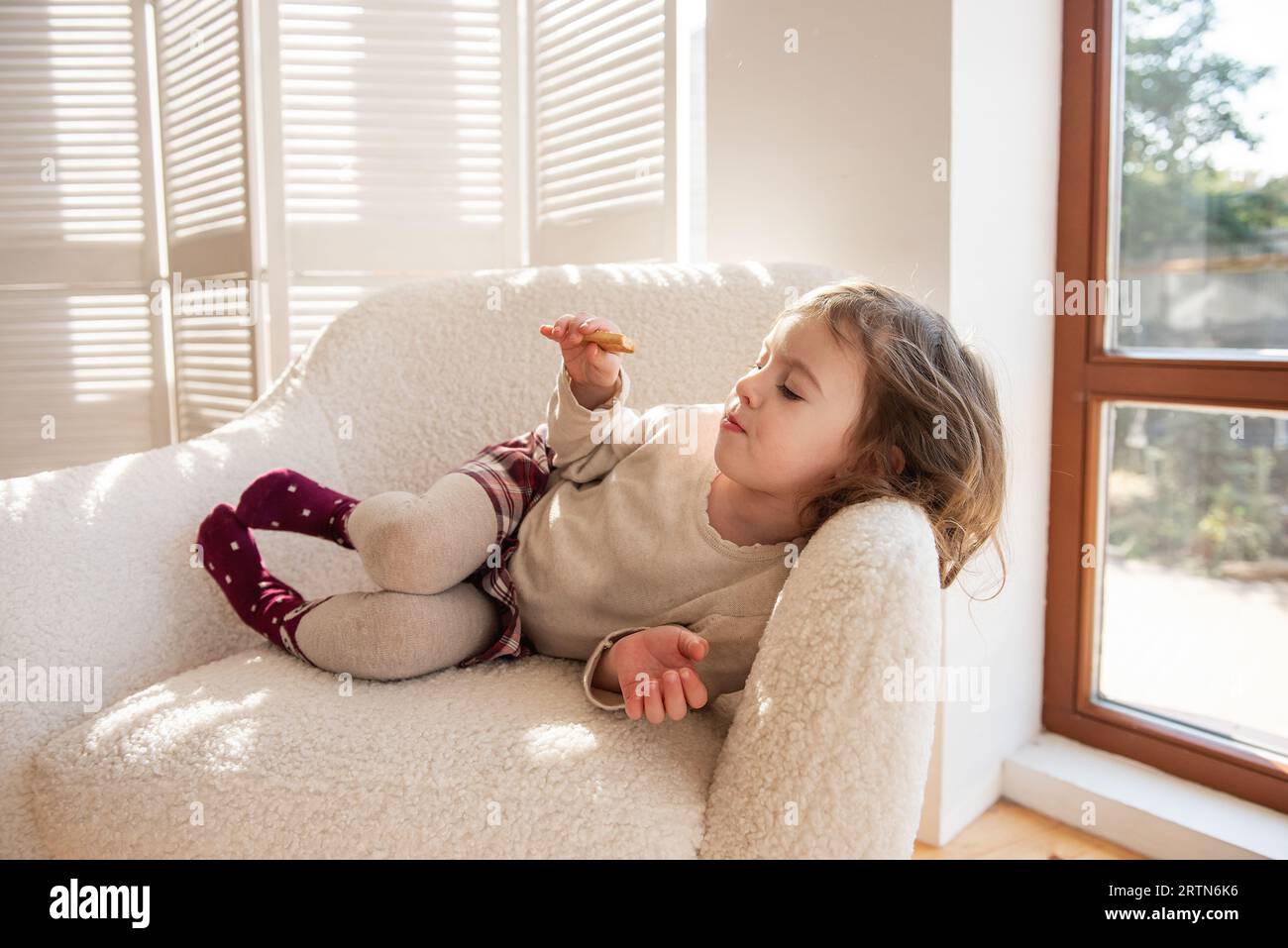Ein nachdenkliches, träumendes kleines Mädchen liegt in einem weichen weißen Sessel und träumt von einem Geschenk des Weihnachtsmanns in der Nähe des Weihnachtsbaums. Kind in gemütlicher Atmosphäre im Stockfoto