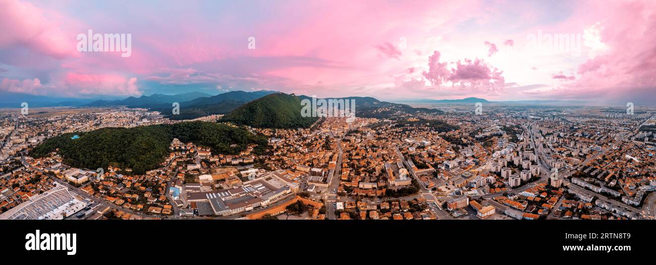 Panoramaaussicht von Brasov bei Sonnenuntergang, Rumänien. Altstadt mit alten Gebäuden, Hügel mit Grünflächen Stockfoto