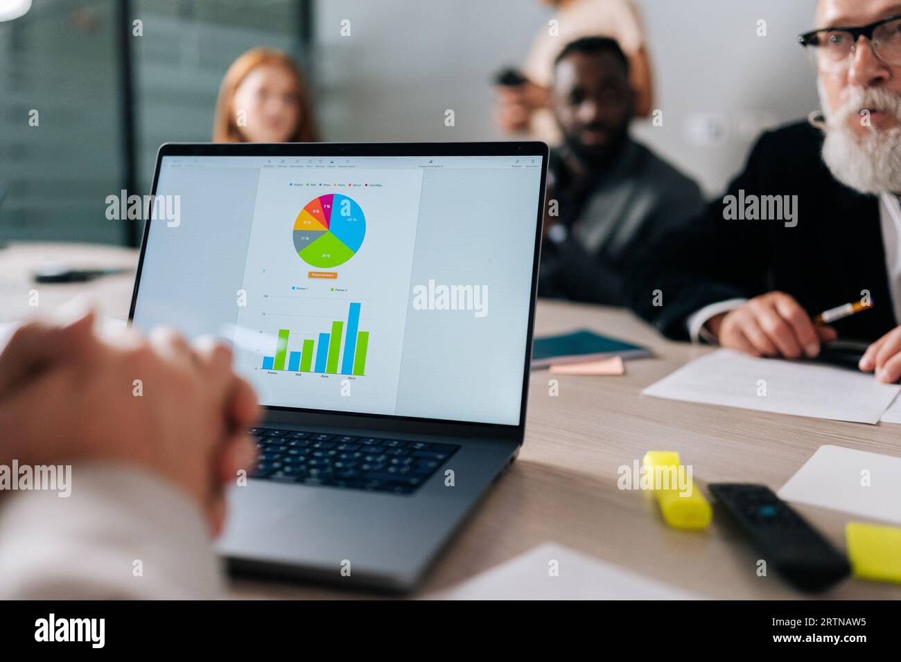 Nahaufnahme vom Laptop mit Diagramm bis hin zur Gruppe verschiedener Geschäftsleute, die sich im Sitzungssaal des Büros treffen, um Geschäfte zu lösen und die Zusammenarbeit mit Partnern zu planen Stockfoto