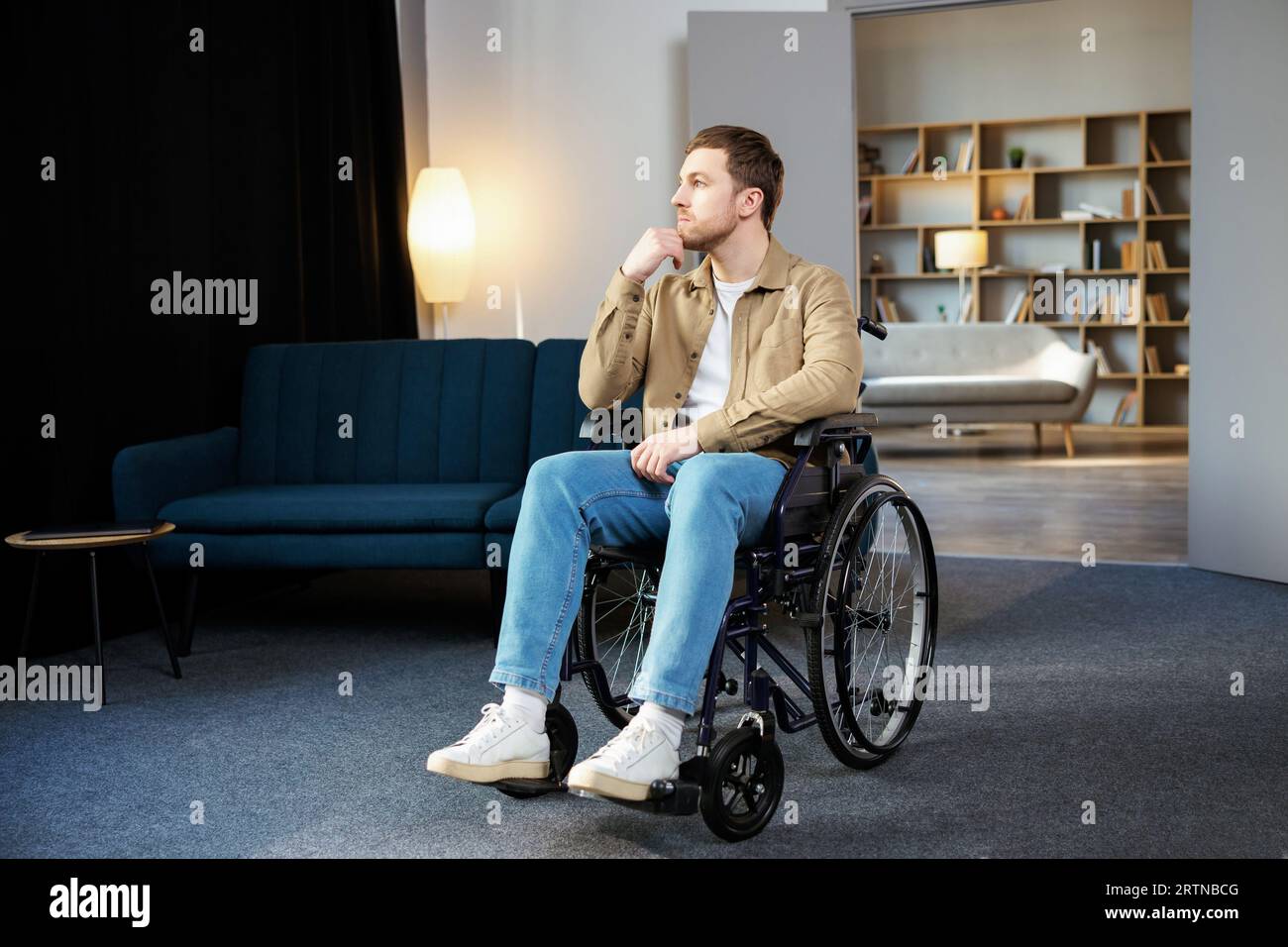 Positive Lebensweise, Betreuung von Behinderten, Rehabilitation und Unterstützung zu Hause. Junger Weißer im Rollstuhl im Wohnzimmer. Stockfoto