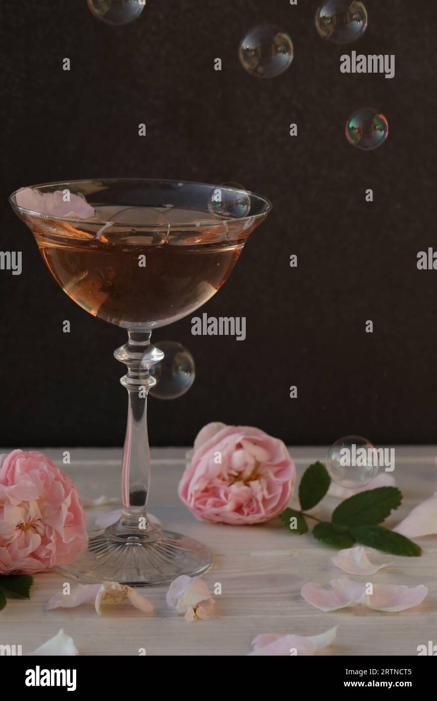 Glas rosa Champagner mit Rosenblüten auf schwarzem Hintergrund Stockfoto