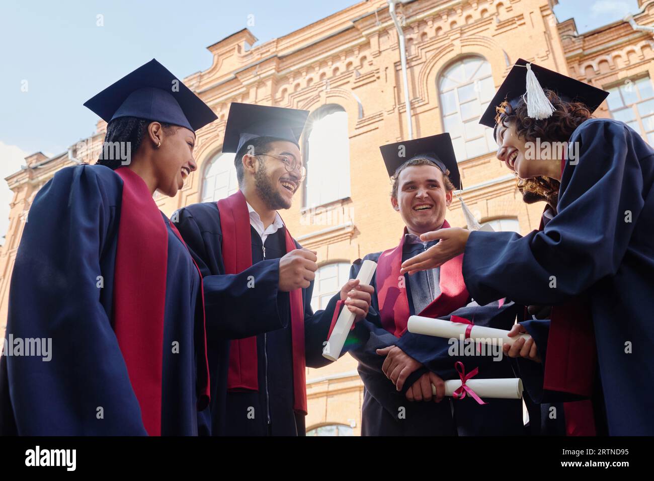 Schwacher Blick auf die glückliche Gruppe von Studenten in Gewändern, die lachen und miteinander reden, während sie auf dem Campus stehen Stockfoto